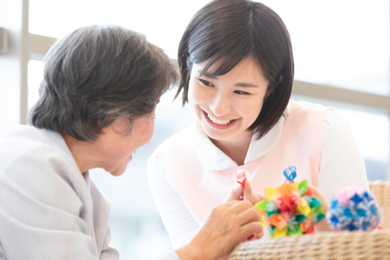 老人ホーム　ボランティア‐折り紙をする高齢者と介護士