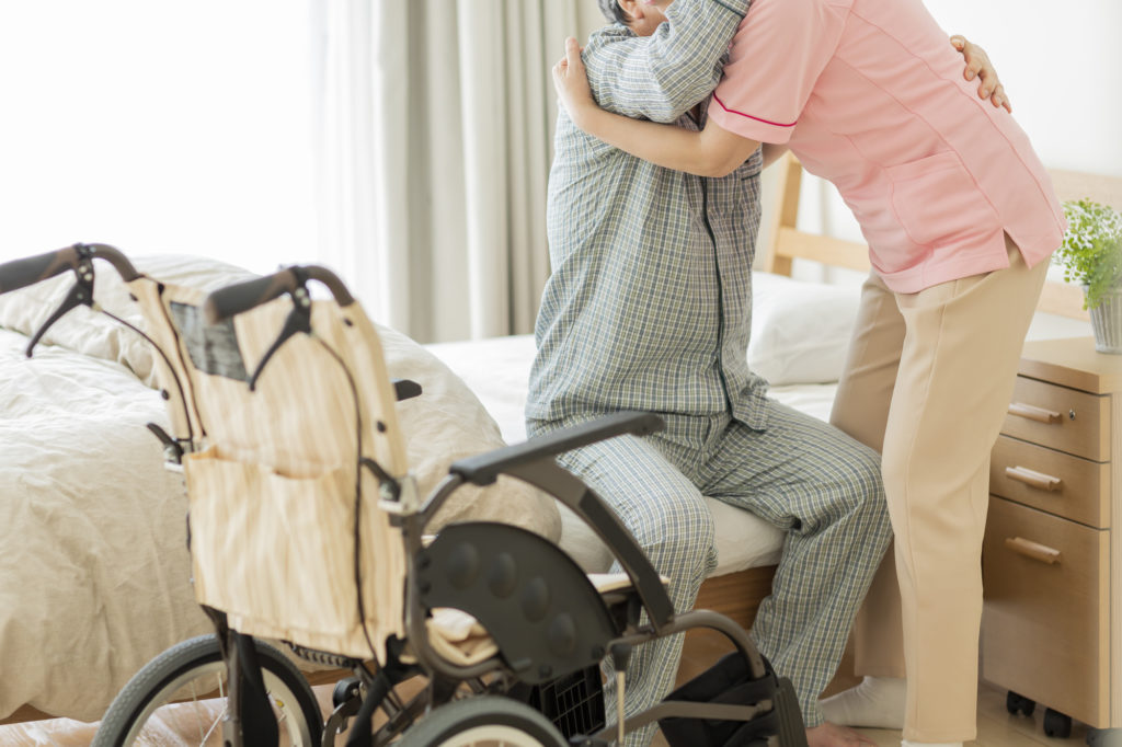 ニチイ　介護施設-ベットから起き上がる時に介護されている高齢者