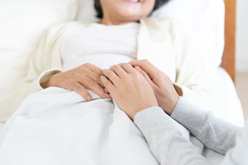 ベッドに横たわるシニア女性の手を握る
